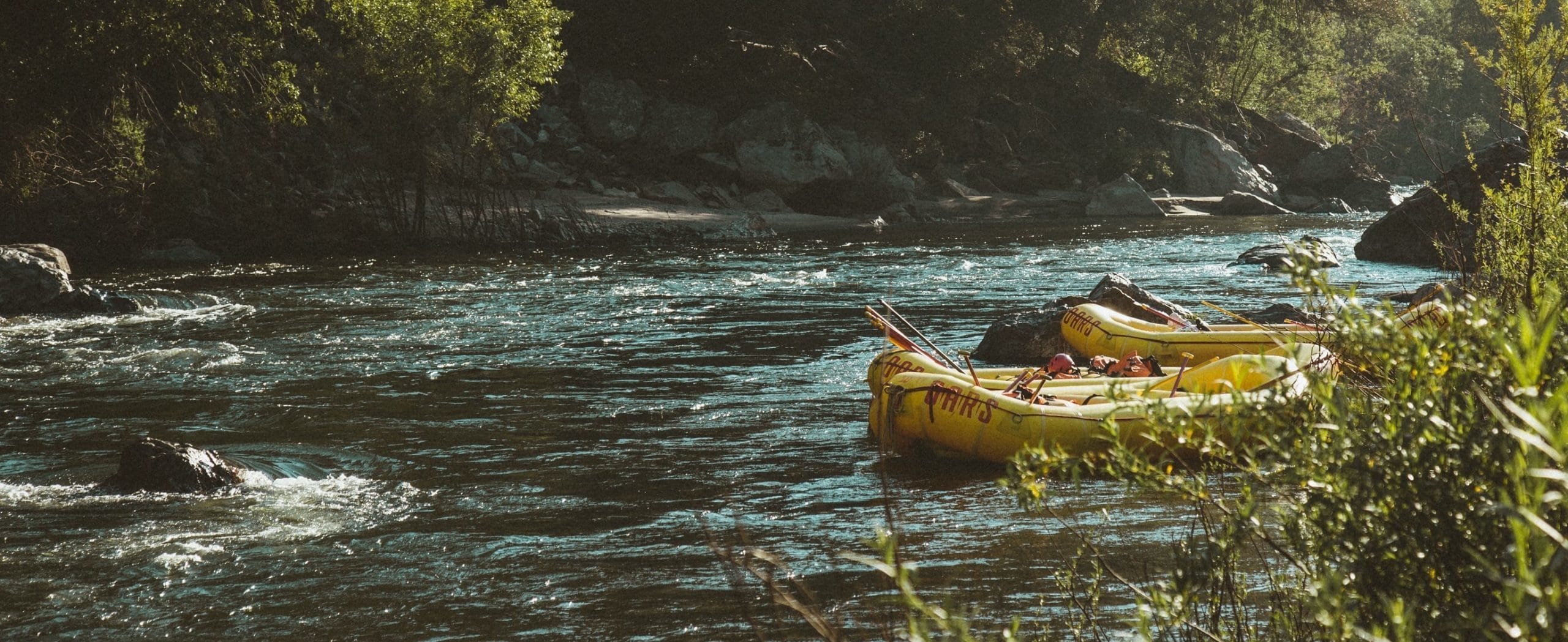 Rafts tied up along shoreline with water rushing and trees