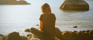 Woman meditating in front of water at sunset.