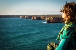 Woman practicing breathwork and meditation while sitting on a cliff overlooking the water and sunset