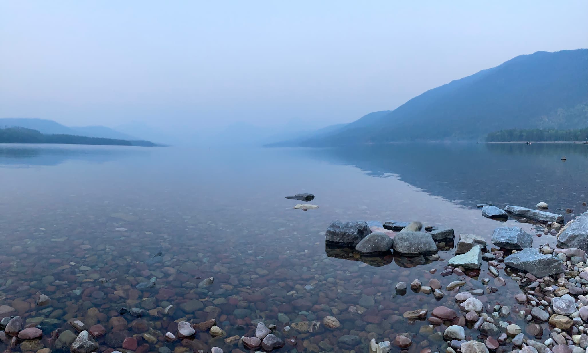 Clear lake in Glacier National Park with fog and mountains in the background