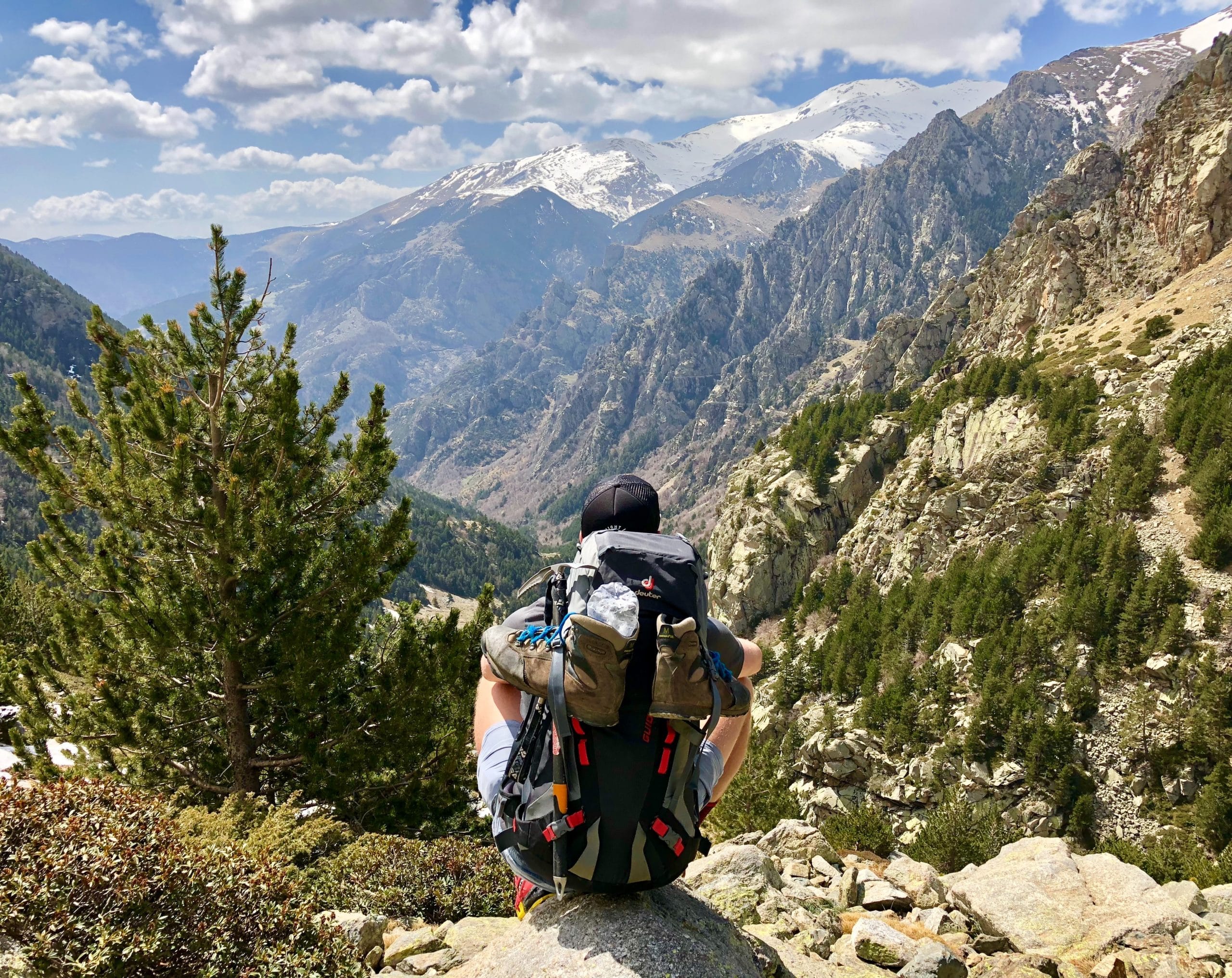 Man with a backpack practicing mindfulness while looking at a valley, trees, and mountains in the distance.