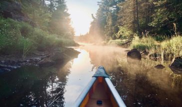 A canoe floating on clear water with fog coming up from it in the Boundary Waters Canoe Area