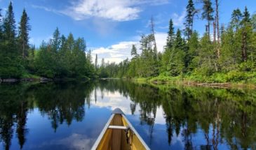 A canoe floating on clear water and blue sky with beautiful trees in the Boundary Waters Canoe Area