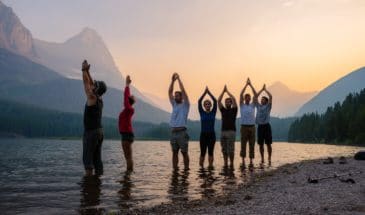 People in a lake with mountains behind them doing mountain pose at sunset