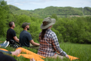 People seated doing a breathwork meditation in the grass overlooking a hill and trees - recal coaches