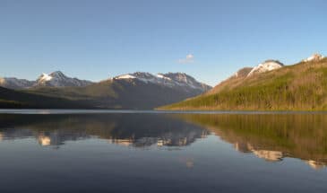 Still water of Lake Kintla with reflection of mountains and a clear blue sky above