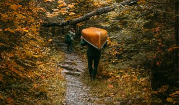 A man portaging with his canoe and a woman with a backpack in the forest