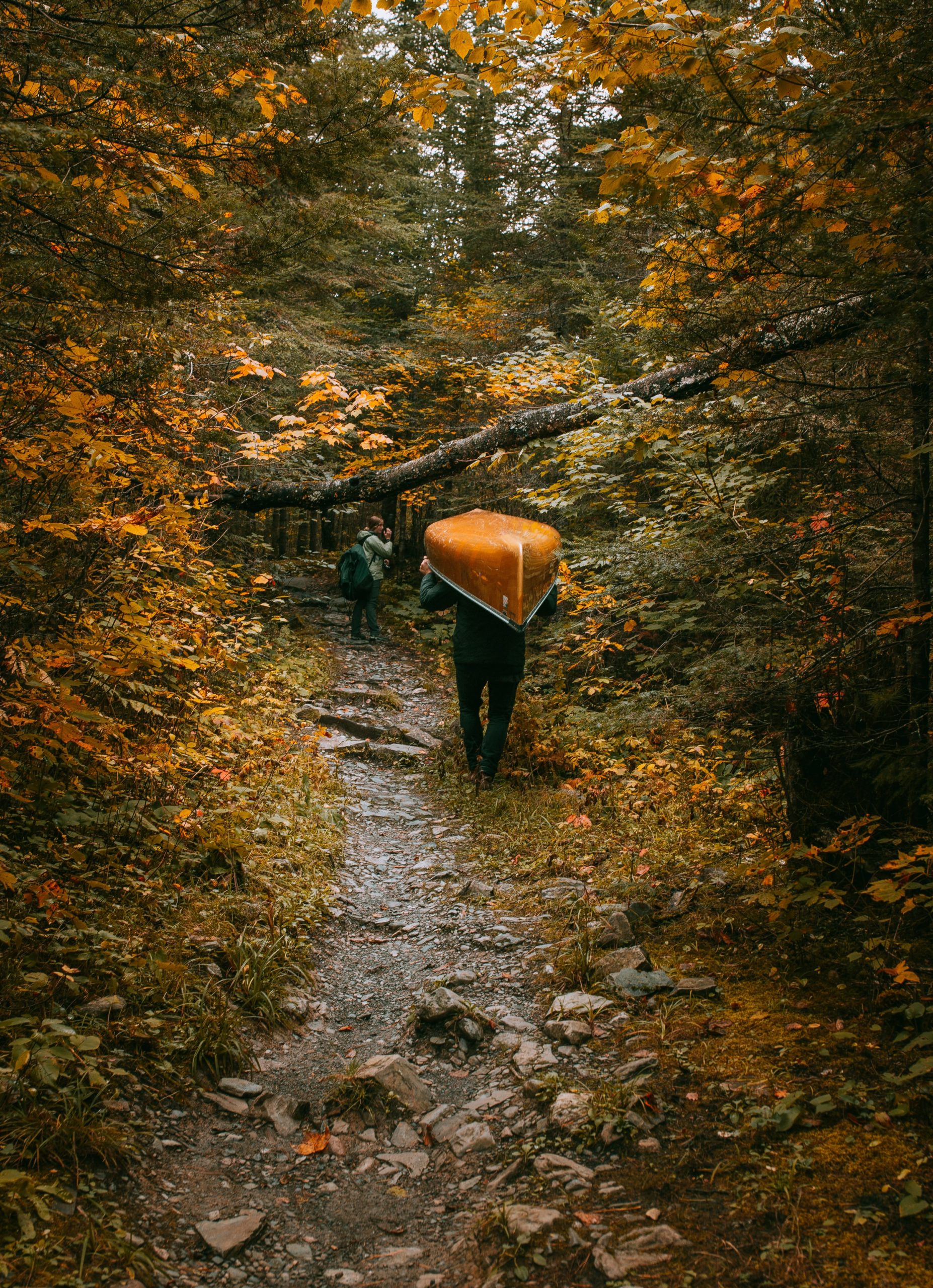 A man portaging with his canoe and a woman with a backpack in the forest