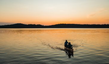 Two people canoeing on a lake at sunset with trees in the background