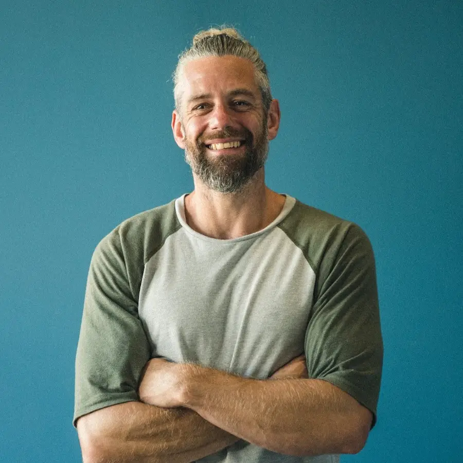 Man smiling and standing with arms folded in front of a blue wall.