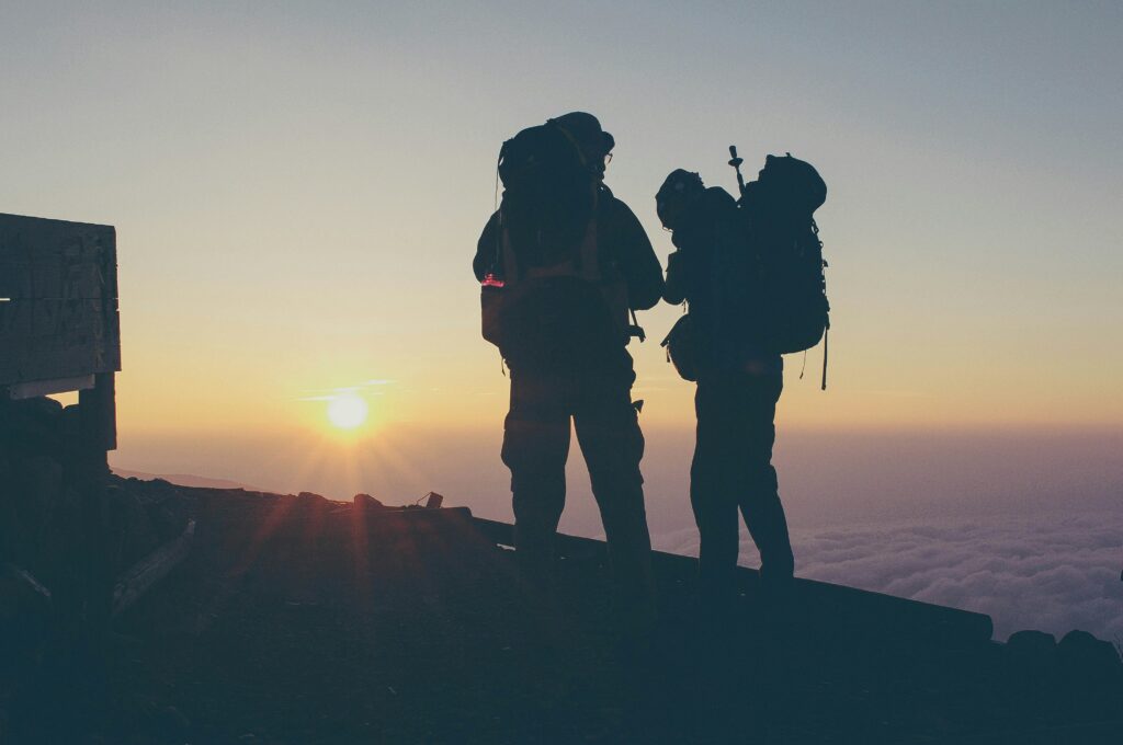 Two people on the summit of a mountain at sunrise with big backpacks and equipment.