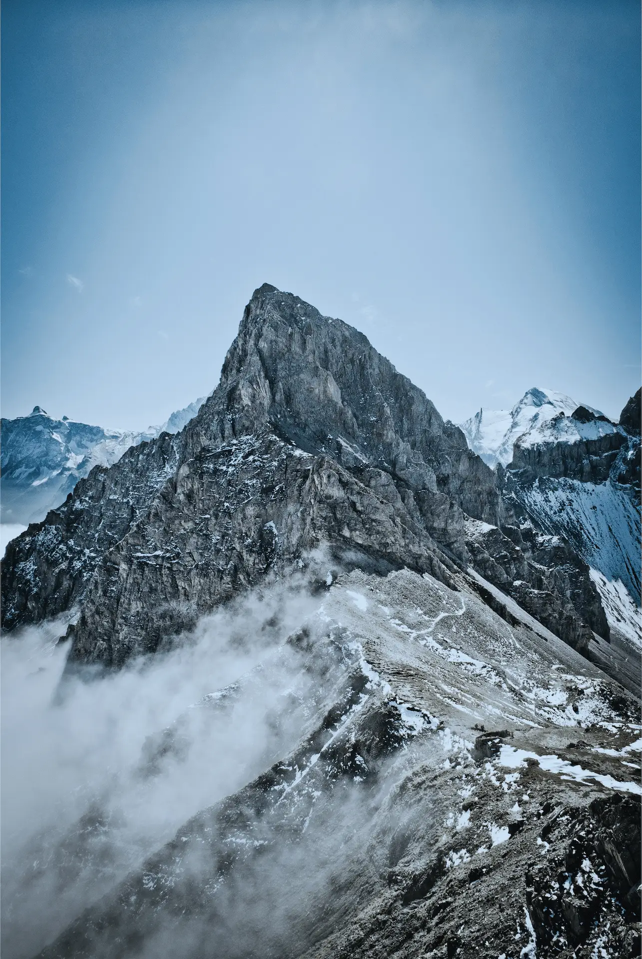 A rocky mountain peak with white snow and clouds nearby.