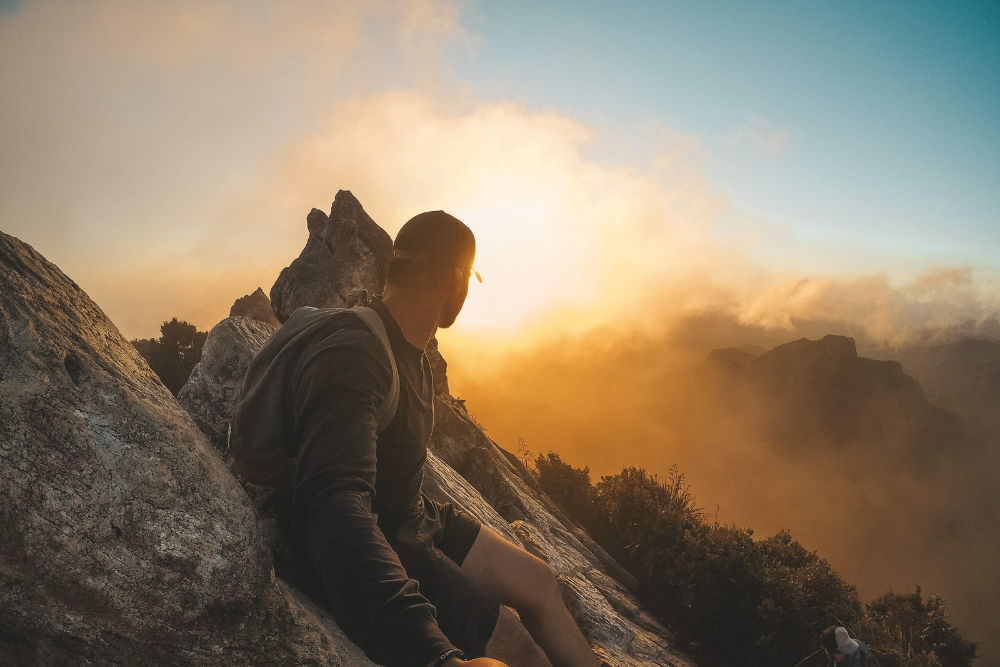 Man sitting on top of the mountain watching the sunset